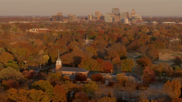 Aerial of a small church surrounded by trees with a downtown city skyline on the horizon