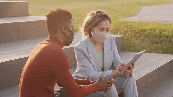 Interracial Business Partners in Face Masks Discussing Work Outdoors