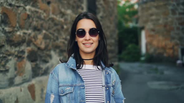 Slow Motion Portrait of Beautiful Young Woman in Sunglasses and Denim Jacket Standing Outdoors with