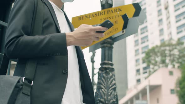 Young Asian businessman using smartphone while standing in the street of the modern city.