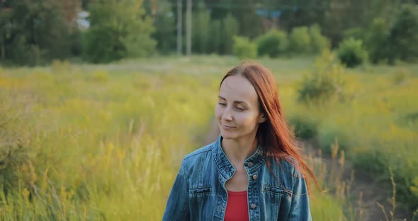 Young Beautiful Woman Walks Along a Forest Road and Touches the Grass with Her Hands