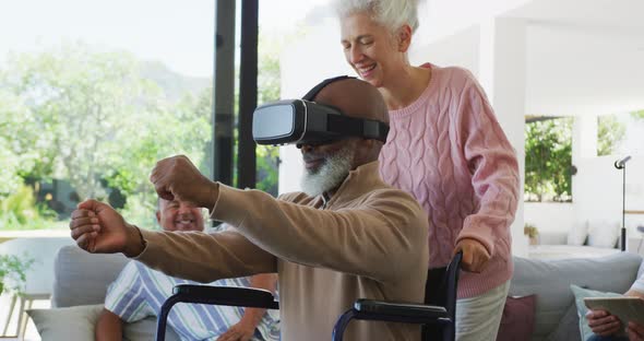 Happy senior diverse people with man in wheelchair using vr headset at retirement home