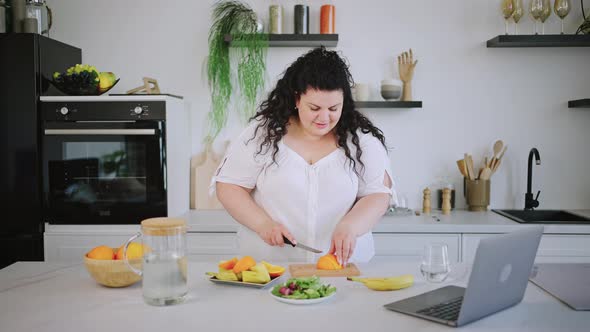 Young Brunette Cuts Orange and Puts on Plate with Vegetables