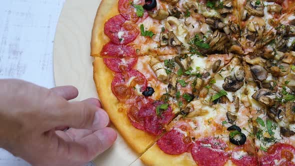 Pizza with Salami Close-up on a Wooden Table. A Man's Hand Takes a Slice of Pizza. Slow Motion