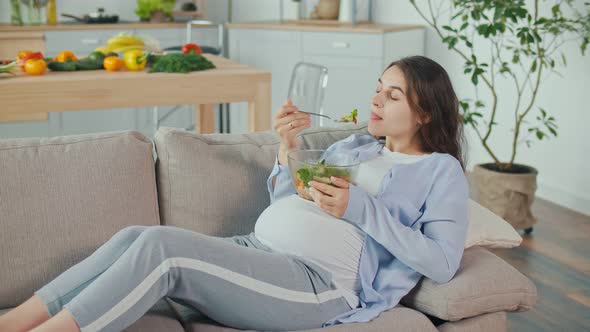 Pregnant Woman With Great Pleasure Eating Vegetable Salad on the Couch