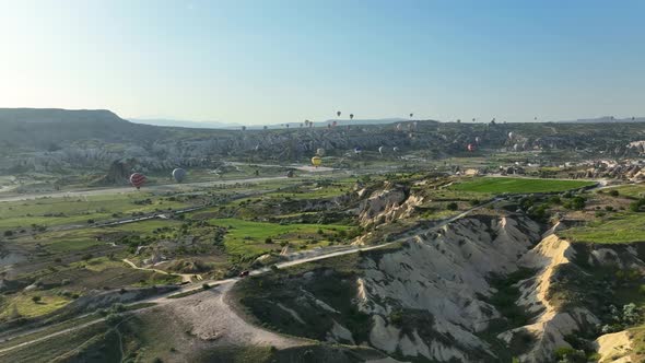 Hot air balloons fly over the mountainous landscape of Cappadocia, Turkey.