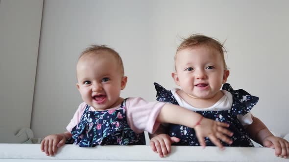 Two fraternal twins sisters having fun in crib. Two babies standing in crib.