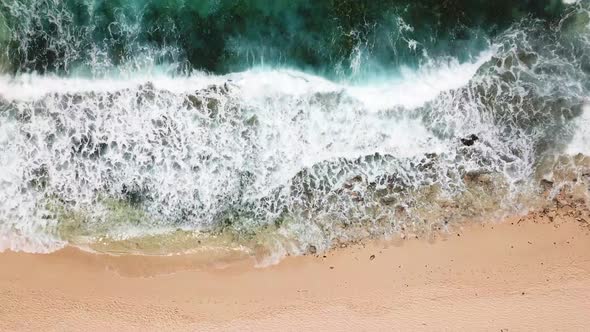 Above vertical view of blue ocean waves and yellow sandy beach