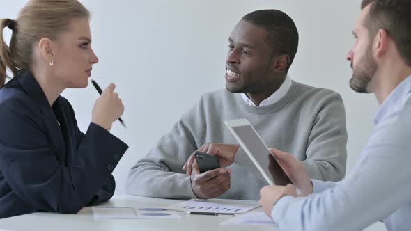 Male and Female Colleagues Discussing While Using Smartphone and Tablet