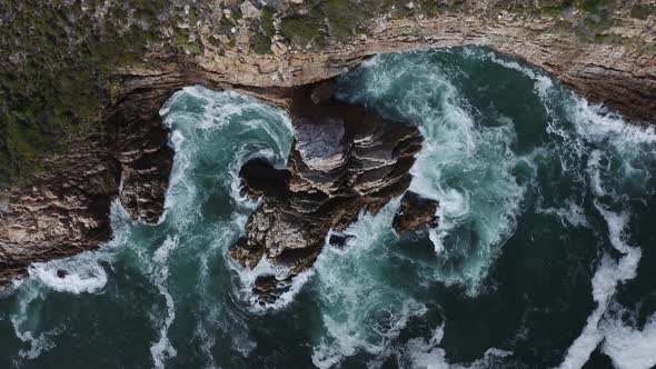 Aerial overhead shot of the Atlantic Ocean breaking on the cliffside shore creating a whirlpool tida