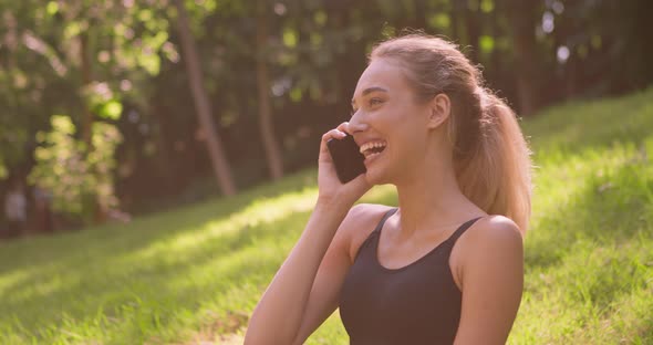 Outdoor Portrait of Happy Young Woman Talking with Boyfriend on Cellphone and Laughing