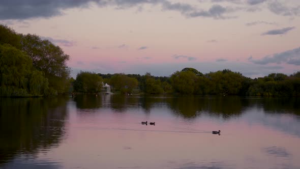 Sunsets over a lake while a lone fisherman casts his line.