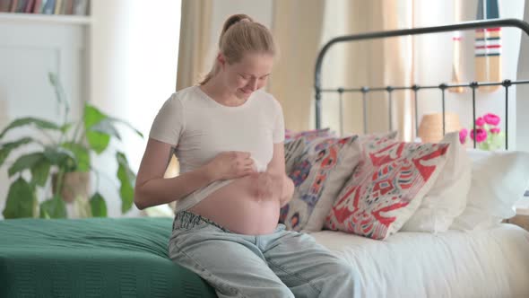 Happy Pregnant Woman Stokes Her Big Belly While Sitting on Bed