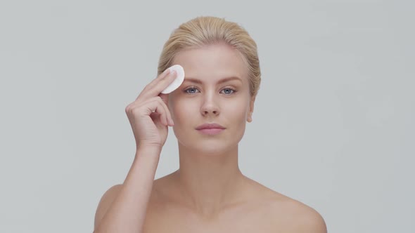 Studio portrait of young, beautiful and natural blond woman applying skin care cream. F