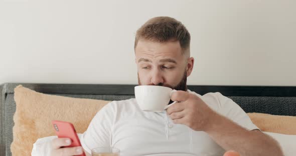 Close Up View of Handsome Bearded Man Drinking Coffee in Bed and Smiling To Camea. Portrait of Happy