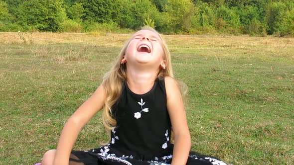 Girl Sitting on the Grass and Bursts out Laughing. Irrepressible Girl's Laugh.