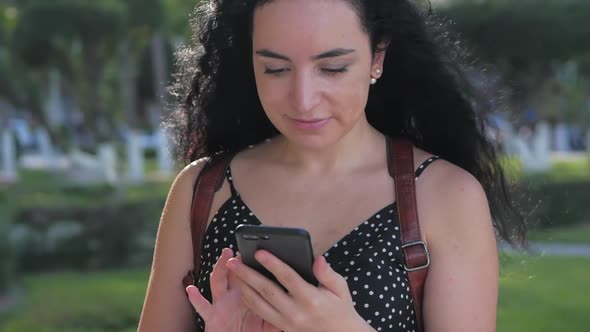 Young Woman or Girl Is Texting Messages on the Phone on a Sunny Day on a Background of Palm Trees