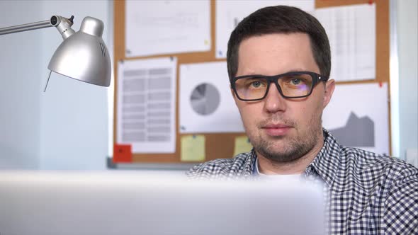 Close Up Shot of a Man Who Works on Laptop in Office with Diagrams on the Wall