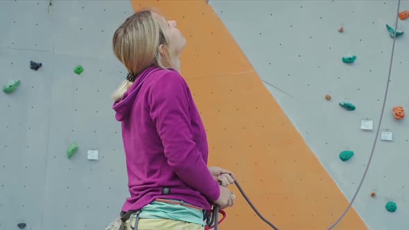 Woman Rock Climber in Yellow Pants Belay with Belaying Device on Rope in Climbing Gym