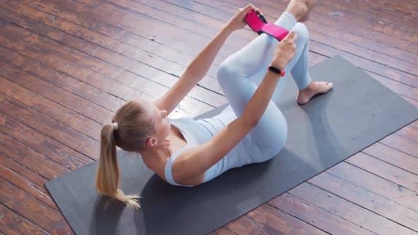 Young and sporty girl in sportswear is using resistance band while doing at home.