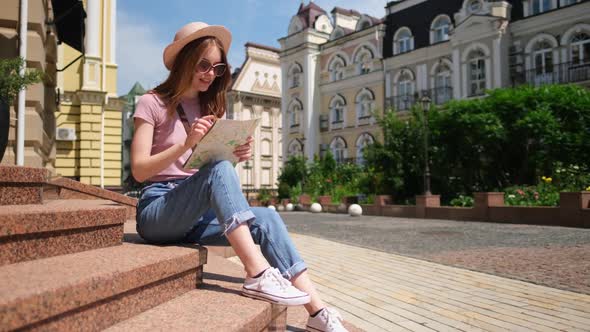 Beautiful Young Woman Tourist Pleasant with City Map Sitting on Stairs in the City Center