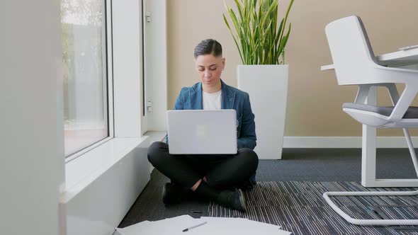 Businesswoman sitting cross-legged in ofice, using laptop