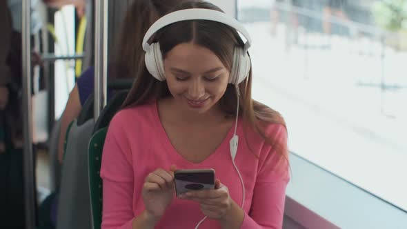 Young Woman Passenger Enjoying Trip at the Public Transport, Sitting with Headphones Near the Window