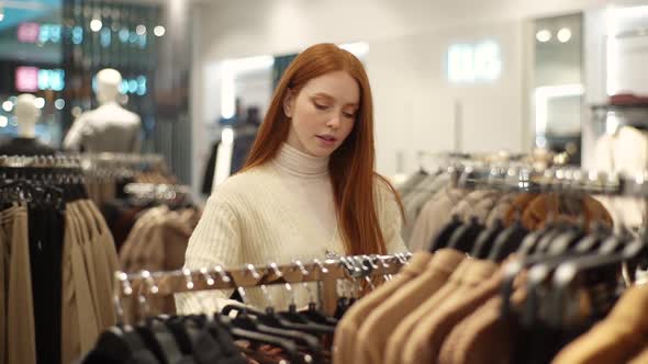 Young Smiling Female Shopaholic Choosing Clothes From Rack in Clothing Store