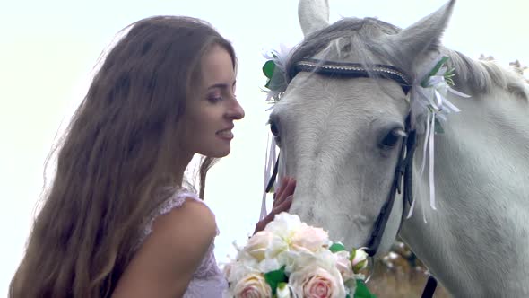 Long-haired Bride in White Wedding Dress Is Posing Near Horse