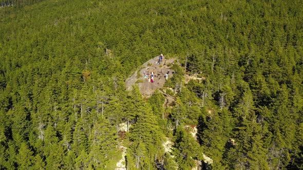 Aerial drone shot over the green and autumn colored forest and a group of hikers on a rocky outcrop