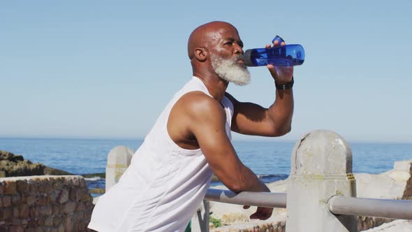 Senior african american man exercising drinking water on rocks by the sea