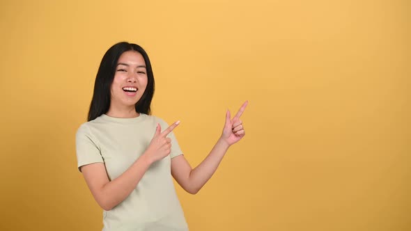Joyful Positive Lovely Brunette Millennial Chinese Young Woman Points with Hands to Empty Space