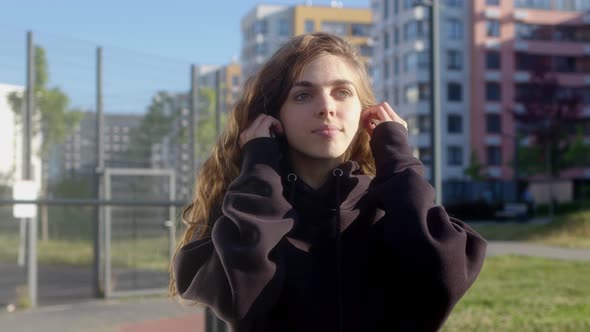 Beautiful Slim Young Woman in Black Sweater Puts on Wireless White Headphones