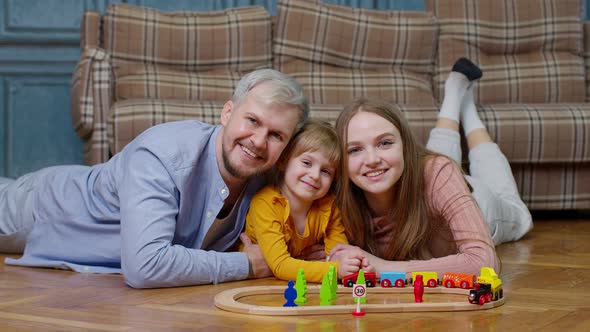 Family of Mother Father with Daughter Child Girl Riding Toy Train on Wooden Railway at Home Room