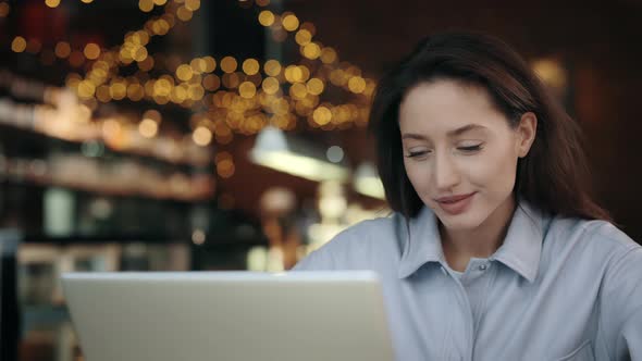 Woman Sitting at Cafe Table and Looking on Laptop Screen