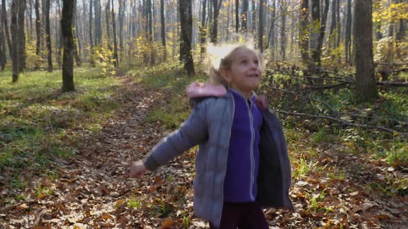 A blond child girl catches and throws a ball in an autumn forest. Nearby lies a dog