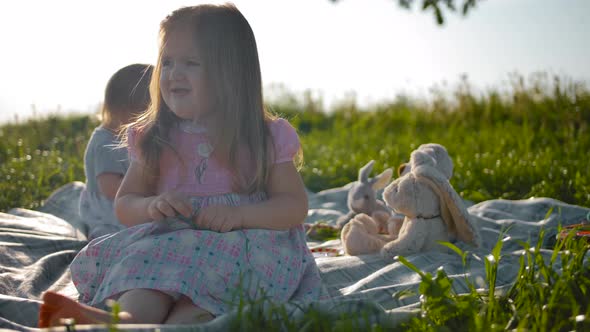 Two Child Sisters Are Sitting on a Picnic Cover.