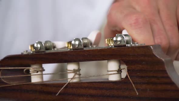 Close up of man moving pegs and tuning acoustic guitar