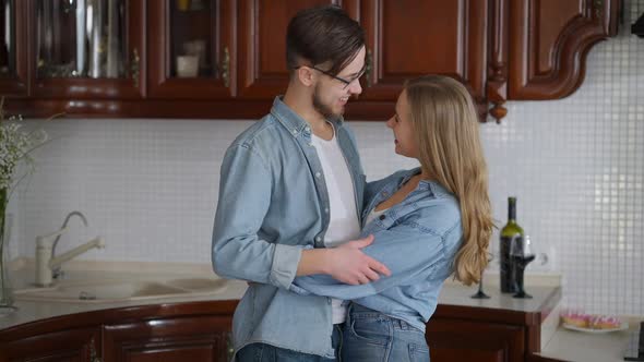 Happy Young Hugging Couple Talking Smiling Turning to Camera Posing in Kitchen at Home