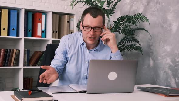 Portrait of a Successful Confident Businessman with Glasses Sitting in the Office at His Desk in