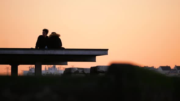 Young couple sitting on the deck enjoying the warm sunset with city in background