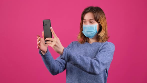 Young Woman Greets Friends During Online Conversation Wearing Medical Mask