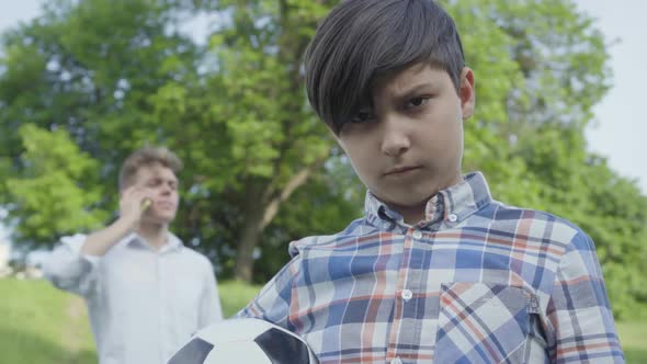 Portrait of a Sad Boy Looking Into the Camera Holding the Soccer Ball in the Foreground. The Young