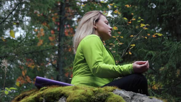 Woman meditating on a rock in the forest