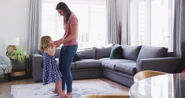 Caucasian mother and daughter having fun dancing in living room