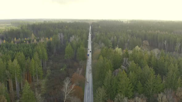 Pullback shot of a drone over a autumn colored forest tracking a transporter car while flying backwa