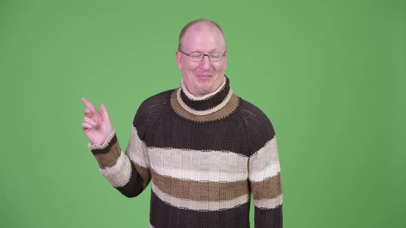 Happy Mature Bald Man with Turtleneck Sweater Laughing While Pointing Finger