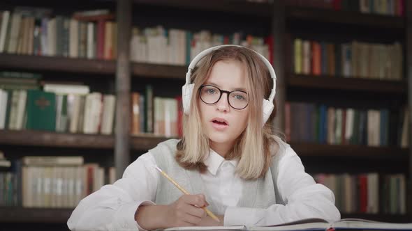 Schoolgirl Pupil Wearing Headphones Writes Notes in a Notebook Distance Learning Online at Virtual
