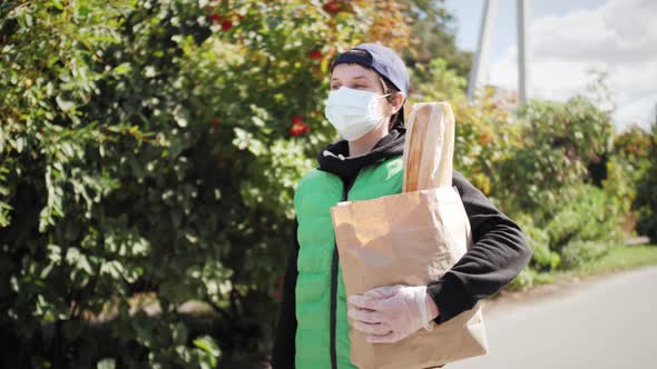 Courier in Protective Medical Mask and Gloves Holding Bag with Foods