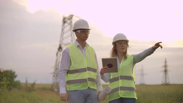 Engineers in Uniform Working with a Laptop Near Transmission Lines